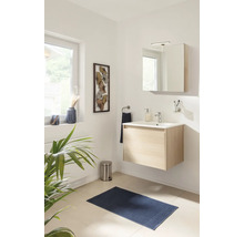 Salle de bain moderne avec meuble sous-vasque en bois clair, lavabo blanc, armoire de toilette, tapis de bain bleu et décoration murale.