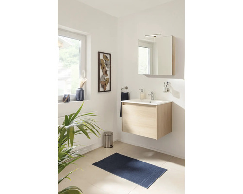 Salle de bain moderne avec meuble sous-vasque en bois clair, lavabo blanc, armoire de toilette, tapis de bain bleu et décoration murale.