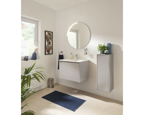 Salle de bains moderne avec meuble sous-vasque suspendu, miroir LED rond, armoire latérale et accessoires assortis dans un design clair.