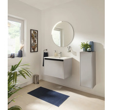 Salle de bains moderne avec meuble vasque blanc, miroir rond et meuble latéral. Inclut un tapis de bain et une poubelle.