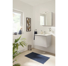 Salle de bains moderne et lumineuse avec un meuble sous-vasque blanc suspendu, une armoire de toilette éclairée et un tapis de bain bleu foncé.