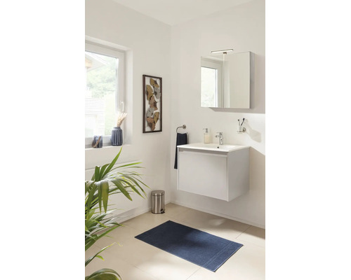 Salle de bains moderne et lumineuse avec un meuble sous-vasque blanc suspendu, une armoire de toilette éclairée et un tapis de bain bleu foncé.