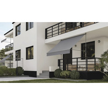Graue Klemmmarkise auf einer Terrasse eines modernen weißen Hauses mit schwarzen Geländern und Garten.