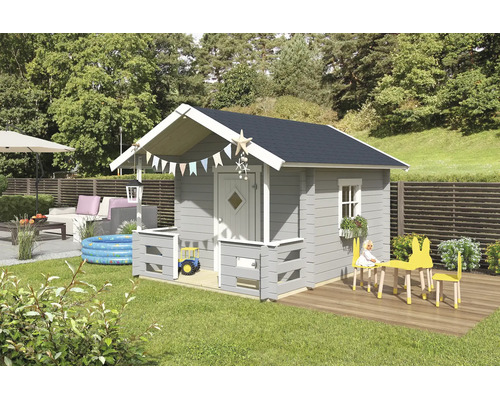 Une cabane pour enfants en bois gris avec toit à pignon, petite véranda et accents blancs dans un jardin lumineux avec jouets et salon de jardin.