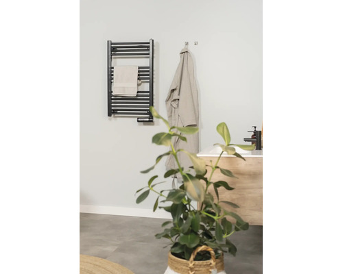 Radiateur sèche-serviettes électrique noir dans une salle de bains moderne avec serviette, peignoir et lavabo.