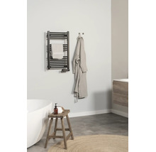 Salle de bains moderne et lumineuse avec un radiateur sèche-serviettes noir au mur, une baignoire blanche, un tabouret en bois et un peignoir.