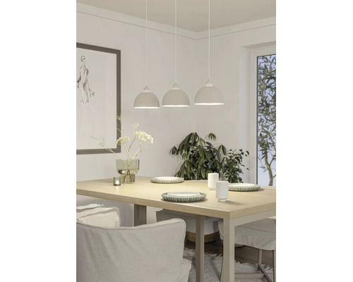 Suspension à trois abat-jour au-dessus d'une table à manger en bois. Salle à manger lumineuse avec vaisselle, vase et grande plante d'intérieur.