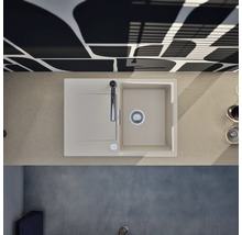 Évier de cuisine moderne avec égouttoir et robinet dans un plan de travail clair, associé à un mur à motifs dans une cuisine lumineuse.