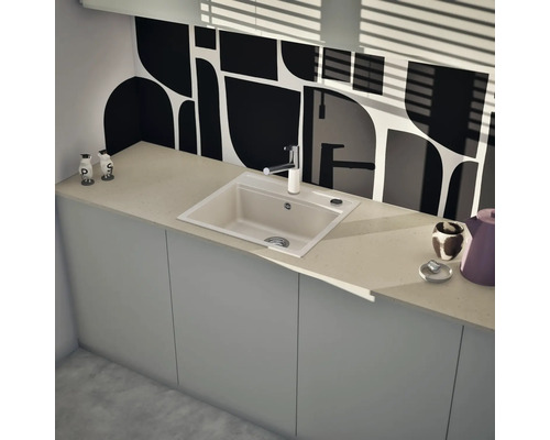 Cuisine moderne avec évier encastré rectangulaire et mitigeur monocommande sur un plan de travail clair devant une paroi à motifs noirs et blancs.