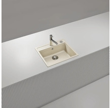 Évier de cuisine encastrable en composite beige avec robinet chromé, installé dans un plan de travail blanc.