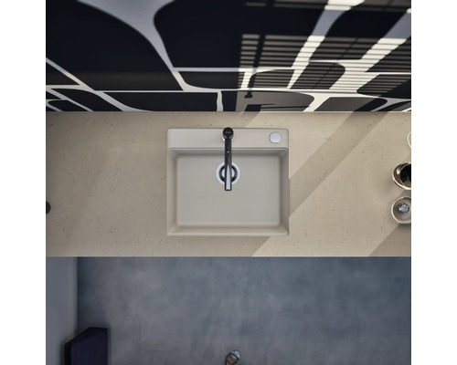 Évier de cuisine moderne avec mitigeur monocommande, vue de dessus sur un plan de travail aspect pierre devant un mur à motifs.