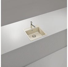 Évier à encastrer beige en composite de quartz avec robinet de cuisine chromé dans un plan de travail blanc.