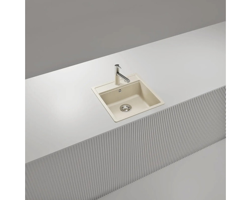 Évier à encastrer beige en composite de quartz avec robinet de cuisine chromé dans un plan de travail blanc.