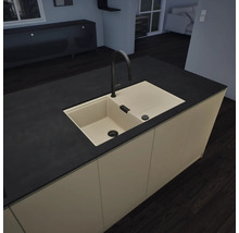 Îlot de cuisine moderne avec évier encastré beige, robinet noir et plan de travail noir dans une cuisine minimaliste et ordonnée.