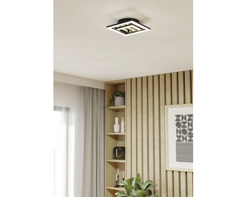 Moderne quadratische LED-Deckenleuchte mit geometrischem Design in einem hellen Raum mit Holzlamellenwand und eingebautem Regal.