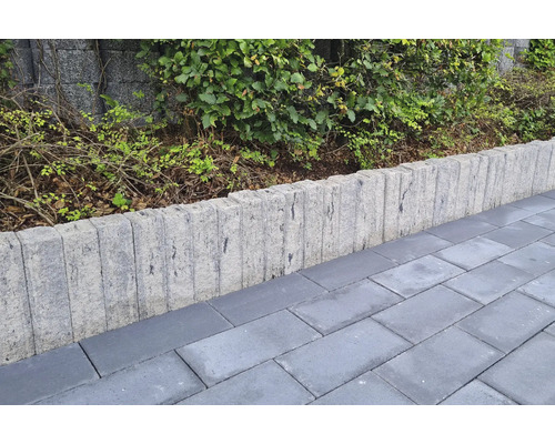 Betonpalisaden als Beetumrandung zwischen einer gepflasterten Fläche und einer Bepflanzung mit Sträuchern.