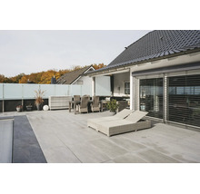 Terrasse moderne avec dalles de sol gris clair, meubles de jardin en rotin clair, chaises longues et pare-vue en verre.
