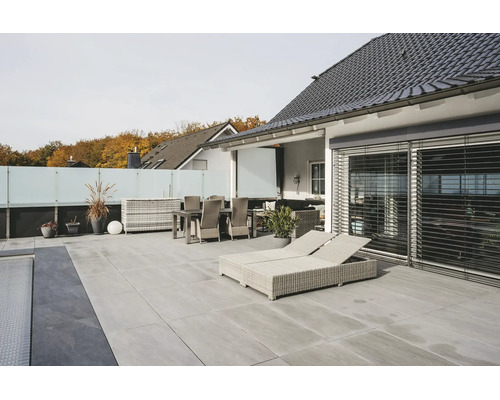 Terrasse moderne avec dalles de sol gris clair, meubles de jardin en rotin clair, chaises longues et pare-vue en verre.