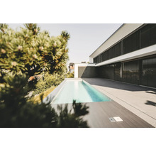 Maison moderne blanche avec stores extérieurs noirs, piscine rectangulaire étroite et vaste terrasse en dalles de pierre grise.
