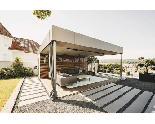 Pergola moderne et lumineuse en métal avec paroi en lattes de bois, rideaux et mobilier de salon sur une terrasse en bois.