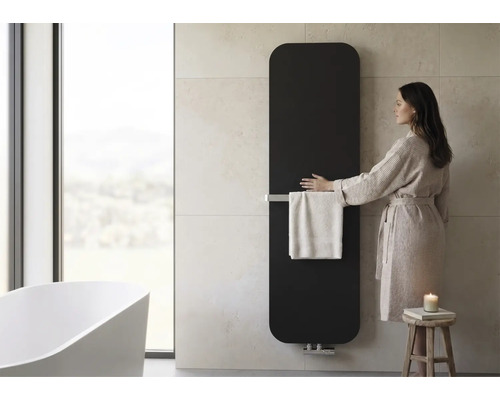 Radiateur de salle de bains vertical avec porte-serviettes dans une salle de bains moderne avec baignoire en îlot et femme en peignoir.