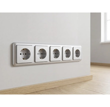 Fünf horizontal angeordnete Schutzkontakt-Steckdosen in einem Rahmen an einer Wand über einem Holzfußboden in einem hellen, organisierten Raum.