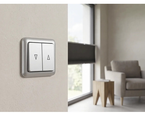Doppelwipp-Rollladenschalter mit Auf- und Ab-Symbolen an einer Wand in einem modernen, hellen Wohnzimmer neben einem Fenster mit Jalousien.