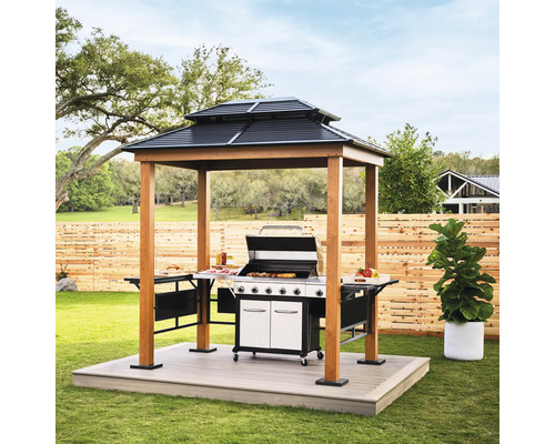 Pavillon de barbecue moderne en bois avec toit en acier à deux niveaux, étagères latérales et barbecue à gaz dans un jardin lumineux.