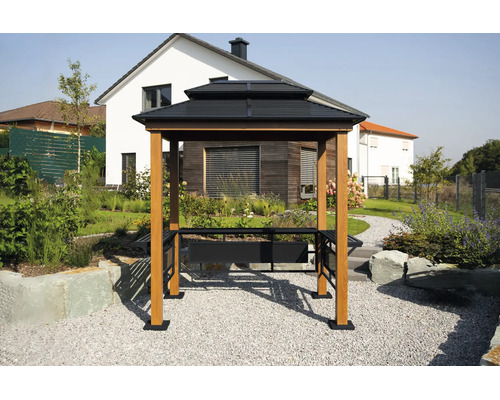 Pavillon de barbecue avec un double toit sombre, des poteaux en bois clair et des étagères latérales dans un jardin devant une maison.