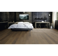 Parquet en lames larges dans une chambre à coucher moderne avec des murs en béton sombre et des meubles industriels.