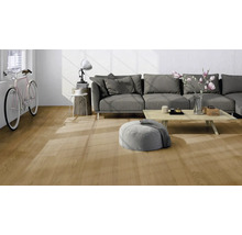 Salon moderne avec un sol clair aspect chêne, un canapé gris, une table basse en bois et un vélo contre le mur.