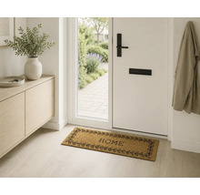 Paillasson en fibres de coco avec texte HOME et motif de feuilles dans une entrée lumineuse.