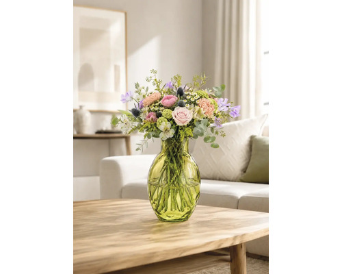 Farbenfroher Blumenstrauß mit Rosen und Eukalyptus in einer grünen Glasvase auf einem Holztisch in einem hellen Wohnzimmer.