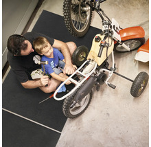 Homme et enfant réparant une moto sur un tapis de protection de sol dans un atelier.