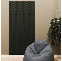 Panneau acoustique noir avec structure ondulée horizontale sur un mur beige, combiné avec un pouf gris et une plante suspendue.