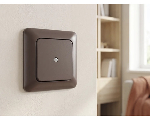 Plaque d'obturation marron en plastique, montée sur un mur clair dans une pièce à vivre lumineuse et organisée.