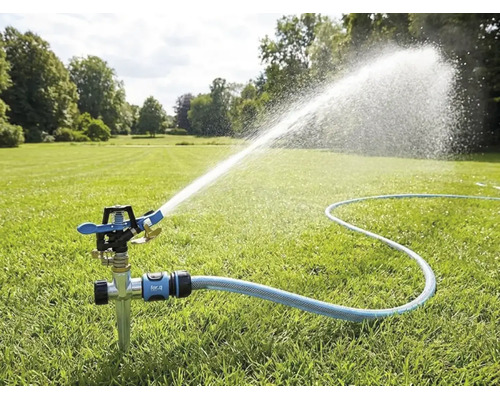 Arroseur par impulsions avec piquet sur une pelouse, raccordé à un tuyau d'arrosage, projetant un jet d'eau pour l'arrosage du jardin.