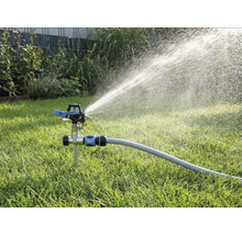 Arroseur à impulsion avec pic sur une pelouse, raccordé à un tuyau d'arrosage, projetant de l'eau en un large jet.