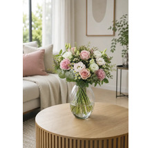 Bouquet de fleurs avec roses et oeillets dans un vase en verre sur une table ronde en bois dans un salon lumineux.