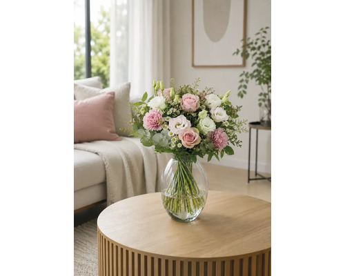 Bouquet de fleurs avec roses et oeillets dans un vase en verre sur une table ronde en bois dans un salon lumineux.