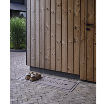 Paillasson avec inscription Schuhparkplatz et un cœur devant une façade en bois sur un sol pavé avec des chaussures.