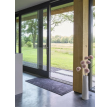 Paillasson rectangulaire à motif de feuilles devant une porte coulissante en verre moderne avec vue sur le jardin et un vase décoratif.