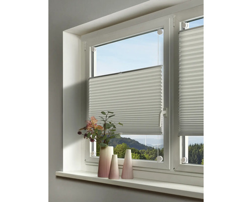 Weißes Plissee an einem Fenster montiert, davor stehen dekorative Vasen auf der hellen Fensterbank.