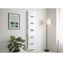 Radiateur vertical moderne blanc avec cinq découpes horizontales, fixé au mur dans une pièce lumineuse avec une plante et un lampadaire.