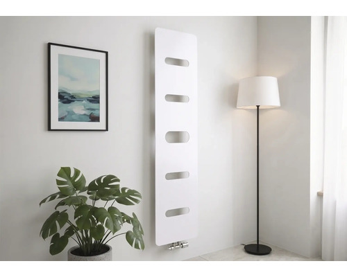 Radiateur vertical moderne blanc avec cinq découpes horizontales, fixé au mur dans une pièce lumineuse avec une plante et un lampadaire.