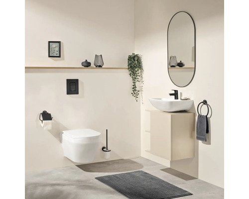 Salle de bain moderne avec WC suspendu, vasque à poser blanche sur meuble sous-vasque beige, robinetterie noire, miroir ovale et tapis gris.