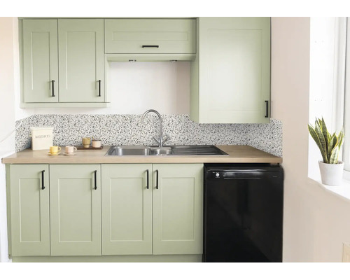 Cuisine moderne avec façades vert sauge, poignées noires, crédence effet terrazzo, évier en inox et plan de travail aspect bois.