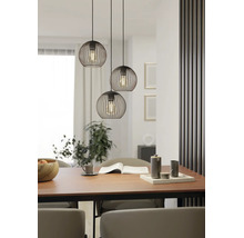 Suspension à trois lampes avec abat-jour en fil de fer noir en forme de sphère au-dessus d'une table à manger en bois dans une salle à manger moderne.