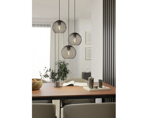 Suspension à trois lampes avec abat-jour en fil de fer noir en forme de sphère au-dessus d'une table à manger en bois dans une salle à manger moderne.