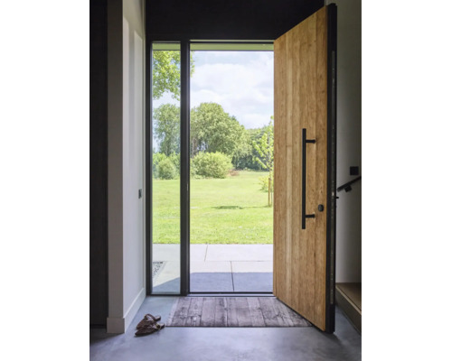 Porte d'entrée ouverte en bois avec poignée barre noire et élément vitré, vue sur une terrasse et une pelouse verte avec des arbres.